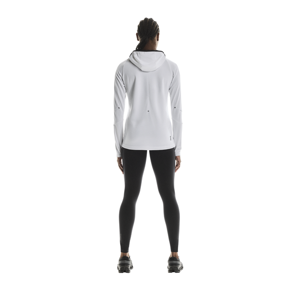 En person ser væk fra kameraet iført en hvid jakke med hætte, On Performance Tights Dame i sort og sorte sportssko på en almindelig hvid baggrund.