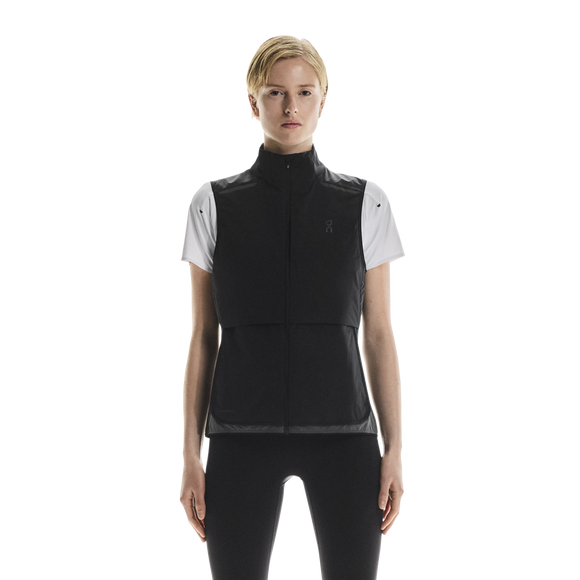 En kvinde ser frem for sig iført On Weather Vest til kvinder i Black/Eclipse over en hvid kortærmet skjorte og sorte leggings på en almindelig hvid baggrund.