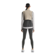 En kvinde kigger væk fra kameraet iført On Weather Vest Dame i Desert/Eclipse - perfekt til beskyttelse mod vejret på løbeturen - over en grå langærmet skjorte, mørkegrå leggings og hvide sneakers på en almindelig hvid baggrund.
