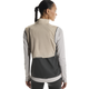 En kvinde med mørkt flettet hår ses bagfra iført On Weather Vest, Dame, i Desert/Eclipse (beige og mørkegrå) over en lys langærmet skjorte - perfekt vejrbeskyttelse løb.