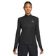 En kvinde iført en sort Nike ACG Half Zip Running Top, Dame, Black/Black/Summit White med huller til tommelfingrene og et lille trekantet logo på venstre bryst, står med front mod en hvid baggrund.