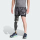 En mand står med front mod en grå skjorte og Adidas Otr Sd 2In1 M herre løbeshorts (Grefou/Black), med blå løbesko og en sort protese på venstre ben, på en almindelig baggrund - perfekt til herre træning.