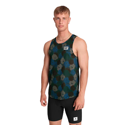 En ung mand står på en ensfarvet baggrund iført Saysky Flower Combat Singlet, Herre, Blue Aop - en mørk mønstret løbeundertrøje - og sorte, tætsiddende shorts. Han ser fremad med et neutralt udtryk og armene langs siden.
