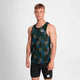 En ung mand står på en ensfarvet baggrund iført Saysky Flower Combat Singlet, Herre, Blue Aop - en mørk mønstret løbeundertrøje - og sorte, tætsiddende shorts. Han ser fremad med et neutralt udtryk og armene langs siden.