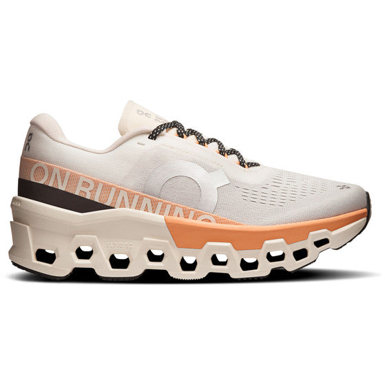 On Cloudmonster 2 Dame Ivory/Tangerine har en tyk geometrisk sål med store udskæringer, responsivt Helion-superfoam, en overdel i beige og orange mesh, sorte og hvide snørebånd og "ON RUNNING" langs siden.