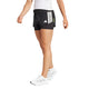 En person er iført en hvid skjorte, Adidas Adizero 2I1 Shorts, Dame i sort med hvide striber, og hvide sneakers på en almindelig lys baggrund. Kun den nederste halvdel er synlig. Ideel til løb med behageligt kompressionsmateriale.