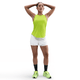 En person står med hænderne på hovedet iført en Nike Dri-FIT Running Tank Top til kvinder i Cyber/Reflective Silver, hvide shorts, sorte knæstrømper og neongrønne sportssko på en almindelig hvid baggrund.