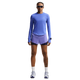 En person står med ansigtet fremad i en Nike Swift UV Long Sleeve Shirt, Dame, Sapphire/Reflective Silv, lilla løbeshorts, hvide sokker, løbesko og solbriller. Håret er flettet, og der er en stor tatovering på venstre ben.