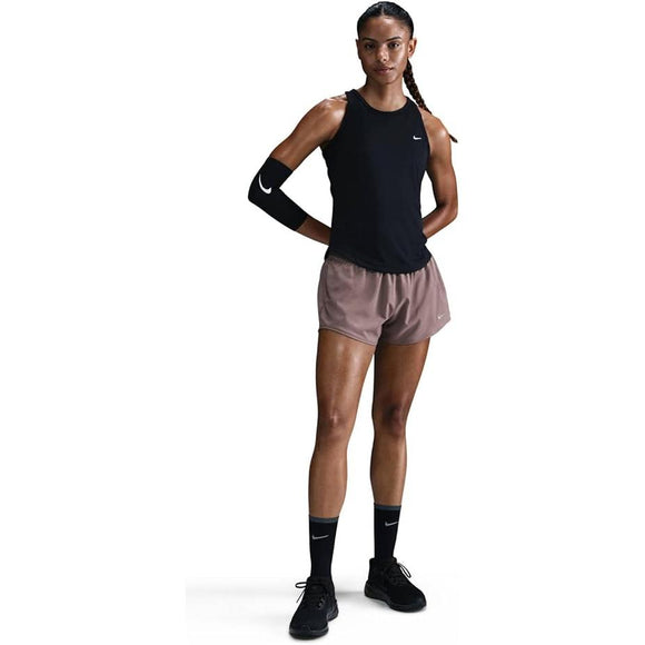 En person står med ansigtet fremad og er iført en Nike Tempo Dri-FIT Running Tank Top (dame, sort), brune sportsshorts, sorte Nike-sokker, sorte sko og et sort Nike-armhylster. Håret er sat op i to fletninger - perfekte løbetøjskvinder.