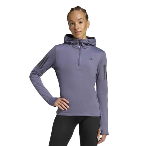 En kvinde kigger fremad iført den lyslilla Adidas Otr Bin Hz Dame Previo træningstrøje med AEROREADY-stof, tre sorte ærmestriber, lynlås foran og logo på brystet - perfekte løbetøj damer sammen med sorte leggings.
