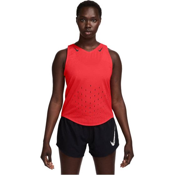 En person står og kigger fremad iført en ærmeløs Nike AeroSwift Singlet, Dame, Lt Crimson/Black/Black med små ventilationshuller og sorte shorts med et hvidt Nike-logo på venstre ben.