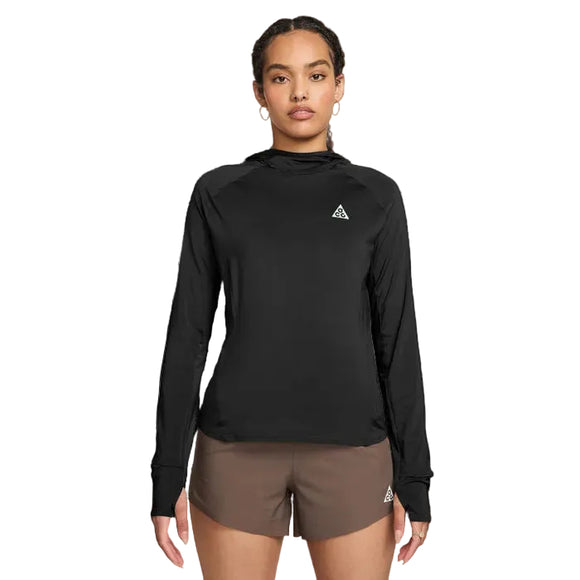 En person kigger fremad i en sort Nike ACG Hooded Mid-Layer Running Top (Black/Black/Summit White, Dame) med et lille trekantlogo og brune sportsshorts med et matchende logo på en hvid baggrund.