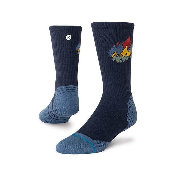 Stance Peaks Ribbed Light Crew unisex-strømperne er marineblå med lyseblå hæl og tå og har geometriske bjergmotiver i rød, gul og grå på siderne.