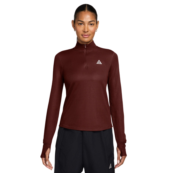 En kvinde iført en Nike Dri-FIT 1/2-Zip Trail Running Top i farven Mystic Dates, med halv lynlås, tommelfingerhuller og et lille logo på brystet.