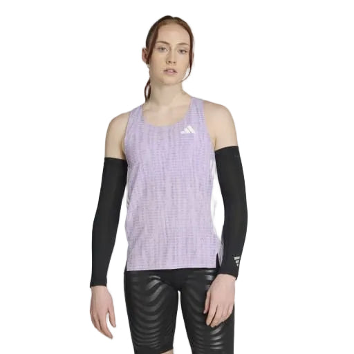 En person med langt, lysebrunt hår, der er bundet tilbage, bærer en Adidas Adizero Singlet Dame i Powplu/Maglil, sorte kompressionsærmer og sorte mønstrede shorts - klar til løb mod en almindelig hvid baggrund.