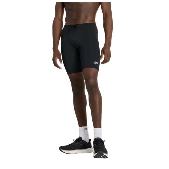 En person er iført New Balance NB Sleek Pocket Half Tight 9" træningstights herre i sort, hvide strømper og sorte løbesko og står på en almindelig hvid baggrund. Kun underkroppen er synlig.