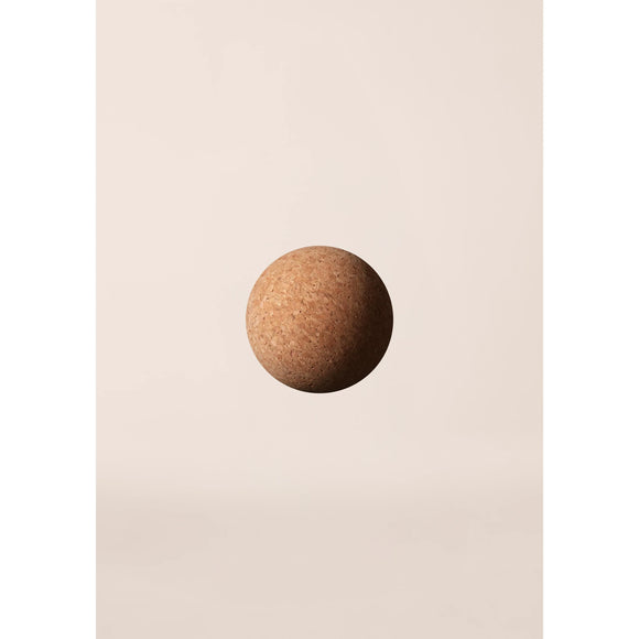 En Casall Pressure Point Ball i naturkork hænger i luften mod en almindelig, lys beige baggrund. Det minimalistiske billede har blød belysning og ingen andre objekter.