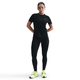 En kvinde iført en sort kortærmet sportstrøje, Nike Therma-FIT ADV High-Waisted 7/8 Reflective Running Leggings i Black/Dk Smoke Grey og neongule løbesko står med ansigtet fremad og hænderne bag ryggen mod en hvid baggrund.