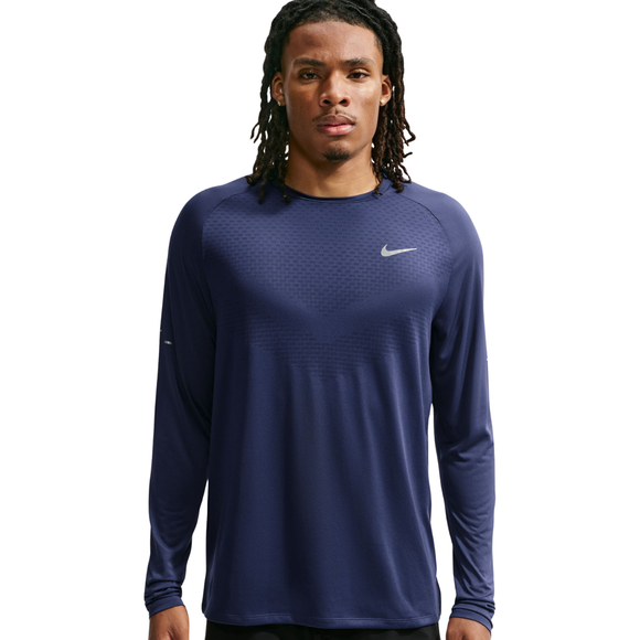 En mand med lange dreadlocks har en Nike Dri-FIT ADV langærmet løbetrøje til mænd i farven Midnight Navy/Reflective Silver på. Han står med ansigtet vendt fremad og et neutralt udtryk på en ensfarvet hvid baggrund.