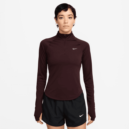 En person ser frem for sig iført en Nike Dri-FIT 1/2-Zip Running Top til kvinder i Burgundy Crush/Reflective Silver og sorte Nike-atletikshorts på en almindelig hvid baggrund.