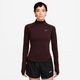 En person ser frem for sig iført en Nike Dri-FIT 1/2-Zip Running Top til kvinder i Burgundy Crush/Reflective Silver og sorte Nike-atletikshorts på en almindelig hvid baggrund.