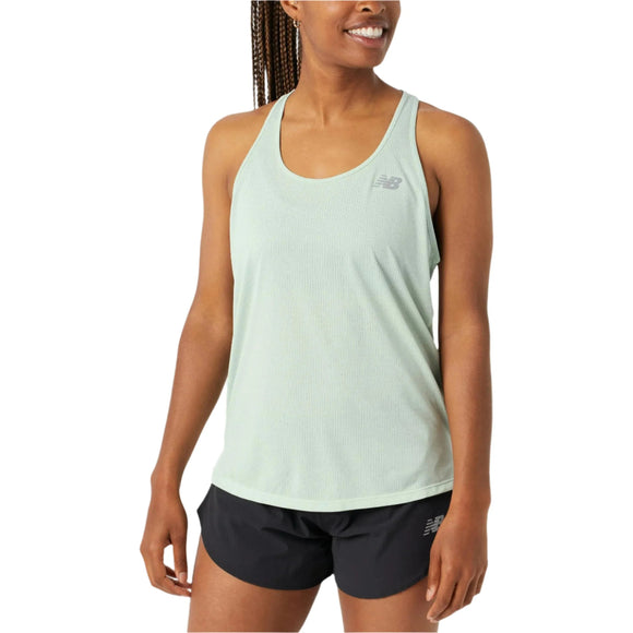 En kvinde iført en lysegrøn Athletics Tank, Dame, Clay Ash Heather fra New Balance og sorte New Balance-shorts står og smiler mod en almindelig hvid baggrund. Ideelle træningstøj kvinder til komfort og stil under enhver træning.