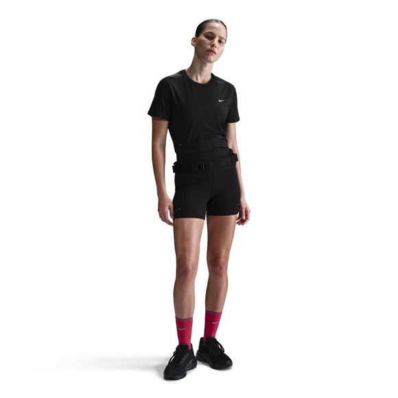 En person står på en hvid baggrund iført Nike Swift SS Running Top til kvinder i sort/reflekterende sølv, sammen med sorte shorts, sorte sko og lyserøde sokker. Håret er trukket tilbage, og armene hviler langs siden.