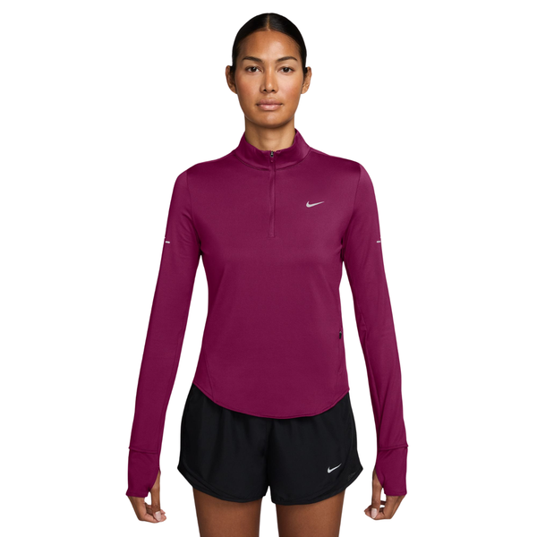En kvinde iført en Nike Swift Half Zip-løbetrøje i farven True Berry/Reflective Silver og sorte sportsshorts.