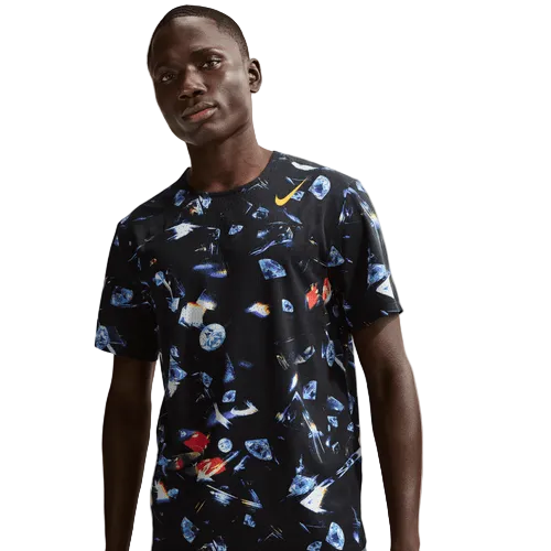 En person iført Nike Aeroswift Aop Ss Running T-Shirt til mænd i Black/Laser Orange med et farverigt abstrakt design og et gult Nike-logo på brystet står på en almindelig lys baggrund.