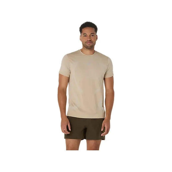 En mand ser frem for sig i en cremefarvet Asics Road Seamless Ss Top for herre og mørkebrune shorts mod en almindelig hvid baggrund.