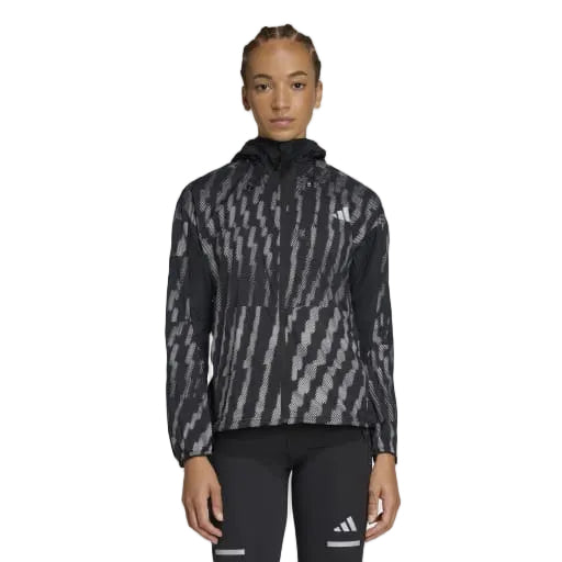 En person iført Adidas Adi365 Jacket, Dame, i Black/Refsil med gennemgående lynlås foran og sorte atletiske leggings står på en almindelig lysegrå baggrund.