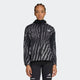 En person iført Adidas Adi365 Jacket, Dame, i Black/Refsil med gennemgående lynlås foran og sorte atletiske leggings står på en almindelig lysegrå baggrund.