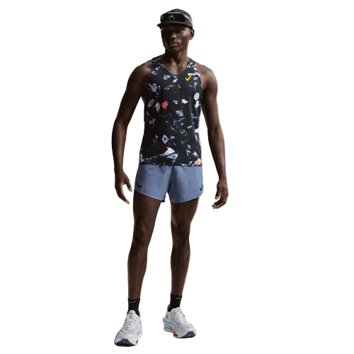 En mand står og kigger fremad iført Nike Aeroswift Singlet Aop, Herre, Black/Laser Orange, lyseblå løbeshorts, hvide sportssko og en sort kasket på en almindelig hvid baggrund.