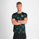 En ung mand med kort blondt hår, iført Saysky Flower Combat T-shirt, Herre, Blue Aop og sorte shorts, står med armene over kors og smiler til kameraet på en almindelig hvid baggrund.