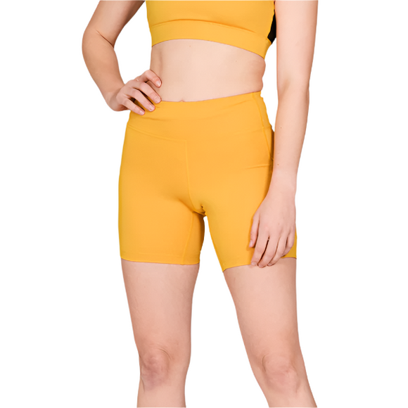 En kvinde iført de gule Saysky W Combat+ Short Tights 7" står med en hånd på hoften mod en almindelig hvid baggrund.