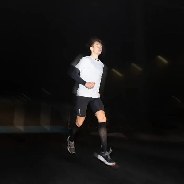 En løber iført LiiteGuard Ground-Tech T-shirt, Herre, White er fanget midt i løbeturen om natten. Den mørke baggrund og det lette bevægelsesslør understreger deres bevægelse.