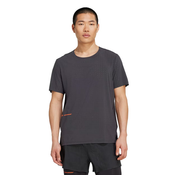 En herre med kort hår står foran en ensfarvet baggrund iført Adidas Adizero x H.Koumori Running T-shirt i sort med diskrete perforeringer, et lille orange logo forneden og sammen med sorte shorts.