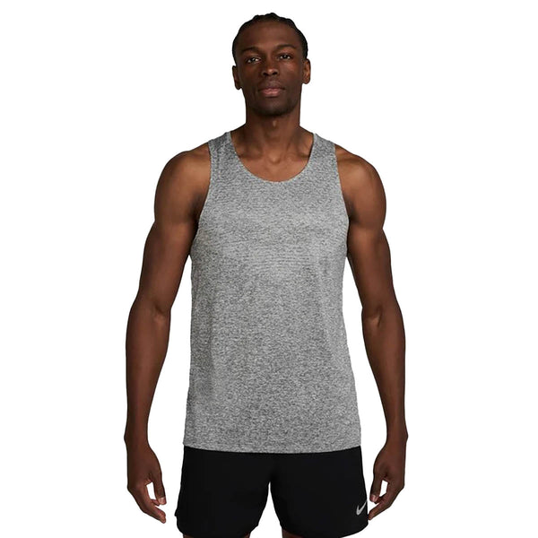 En mand står og kigger fremad iført en Nike Stride Running Tank til mænd i Smoke Grey/Htr/Reflective Silv og sorte Nike-shorts. Baggrunden er helt hvid.