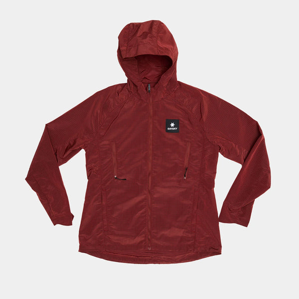 Saysky W Clean Pace Shield Jacket til kvinder i rød har en lynlås foran, to brystlommer med lynlås og et sort mærke med en hvid stjerne og teksten "starter" på venstre bryst, der vises fladt på en hvid baggrund.