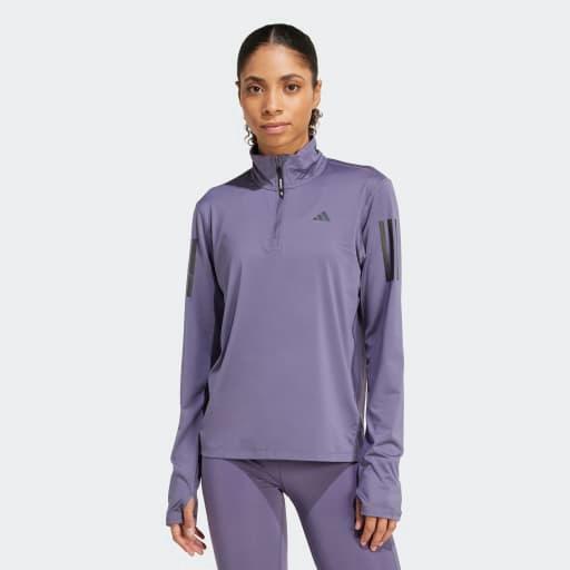 En person iført Adidas Otr B Hzip, Dame, Previo lyslilla quarter zip-top med matchende leggings står med front mod en almindelig hvid baggrund.