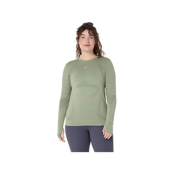 En kvinde i åndbart træningstøj med Asics Road Seamless LS Top for dames i Monument Blue/Whisper Green og mørke leggings står på en almindelig hvid baggrund.