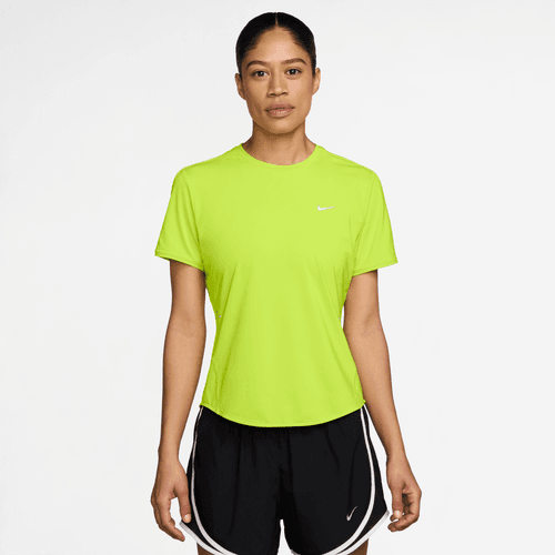 En kvinde kigger fremad i en Nike Dri-FIT kortærmet løbetop til kvinder i Cyber/Reflective Silver, parret med sorte shorts - ideelt reflekterende løbetøj - mod en almindelig hvid baggrund.