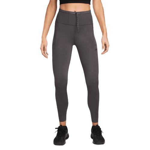 En person i en sort crop top, Nike Trail 7/8 Tights til kvinder i Thunder Grey/Black med sidelommer og sorte sportssko står på en almindelig hvid baggrund. De højtaljede tights er i Dri-FIT-materiale. Personens ansigt er ikke synligt.