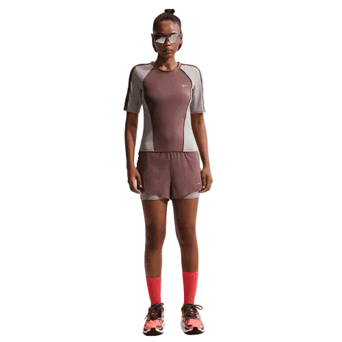 En person ser frem for sig iført solbriller, røde sokker, pink løbesko og en Nike Swift Dri-FIT Short-Sleeve Running Top for dames i Tattoo/Lt Violet Ore/Reflective Silver - et åndbar løbetøj-sæt - mod en ensfarvet baggrund.