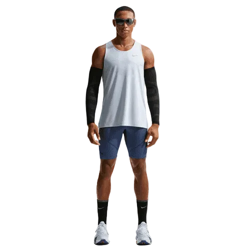 En mand står med front mod solbriller, en hvid ærmeløs sportstrøje, Nike Dfadv Aroswft Bf Htight løbetights (Game Royal/Diffused Blue/Obsidian/Black), sorte ærmer, blå shorts, sorte sokker og hvide løbesko på en hvid baggrund.