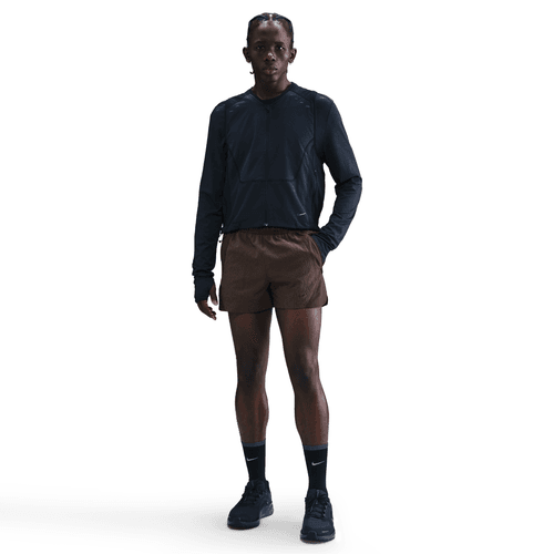 En person står med front mod en hvid baggrund iført en langærmet sort sportstrøje, Nike 5" Dri-FIT ADV Brief-Lined Running Shorts til mænd i Baroque Brown/Black/Blkref, sorte strømper og sorte løbesko.