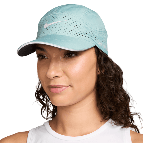 En kvinde i en hvid tanktop bærer Nike Adv Fly Cap Unisex i Cannon/Anthracite/Reflective Silv, med perforerede huller og Dri-FIT-teknologi for komfort, og ser lidt venstreorienteret ud mod en almindelig hvid baggrund.