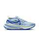 Nike Zegama 2 Dame i LT Armory Blue/Racer Blue vises i sideprofil med en lyseblå overdel, tyk spættet sål, blå swoosh og accenter, hvide snørebånd og et gult Vibram-logo på mellemsålen mod en almindelig hvid baggrund.
