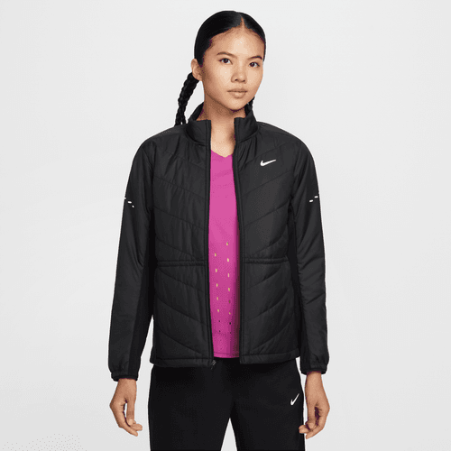 En kvinde med langt flettet hår er iført en sort Nike Therma-FIT løbejakke (Dame, Black/Reflective Silv) over en lyserød skjorte og sorte bukser, mens hun står på en almindelig hvid baggrund.