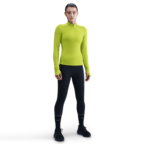 En person står med ansigtet fremad i en knaldgul Nike Therma-FIT ADV 1/2-Zip Reflective Running Top (Dame, Cyber/Reflective Silver), sorte leggings og sorte sportssko på en almindelig hvid baggrund.